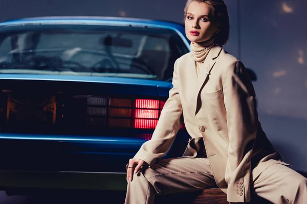 Attraktive und stilvolle Frau sitzt in der Nähe von Retro-Auto und blickt in die Kamera — Stockfoto