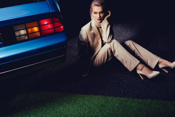 Mujer atractiva y elegante en traje sentado cerca de coche retro - foto de stock