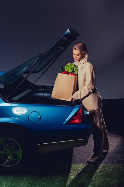 Привлекательная и стильная женщина в костюме упаковки бумажный пакет с едой в багажнике — стоковое фото