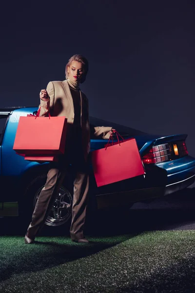Attraktive und stylische Frau im Anzug, die neben dem Retro-Auto steht und Einkaufstüten hält — Stockfoto