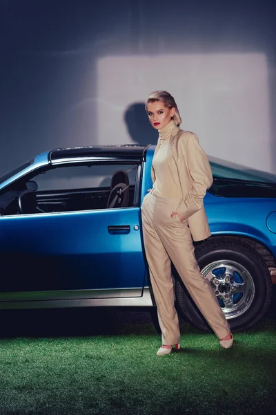 Attractive and stylish woman in suit with hands in pocket standing near retro car — Stock Photo