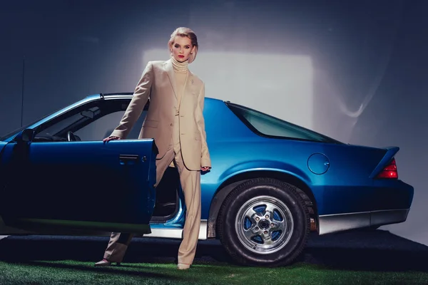 Mujer atractiva y elegante en traje de pie cerca de coche retro - foto de stock