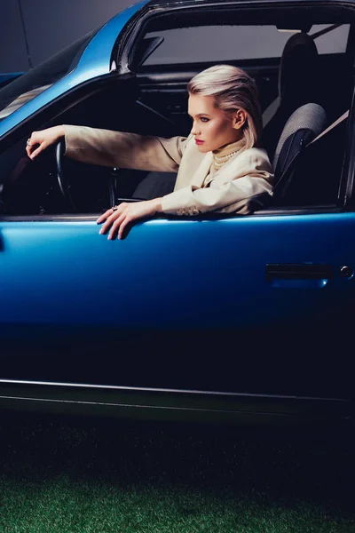 Высокий угол обзора привлекательной и стильной женщины в костюме сидящей в ретро-машине — стоковое фото