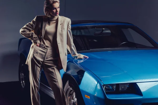 Mujer atractiva y elegante en traje con las manos en la cadera de pie cerca de coche retro - foto de stock