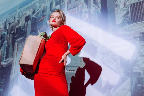 Low angle view of attractive and stylish woman in red dress holding paper bag with food on city background — Stock Photo