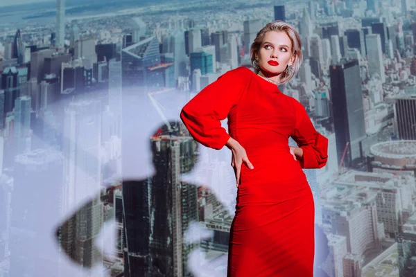 Mujer atractiva y elegante en vestido rojo con las manos en las caderas en el fondo de la ciudad - foto de stock