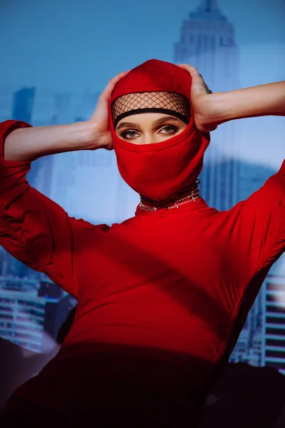 Femme élégante en robe rouge et cagoule sur fond de ville — Photo de stock