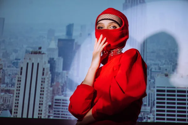 Mujer con estilo en vestido rojo y pasamontañas en el fondo de la ciudad - foto de stock