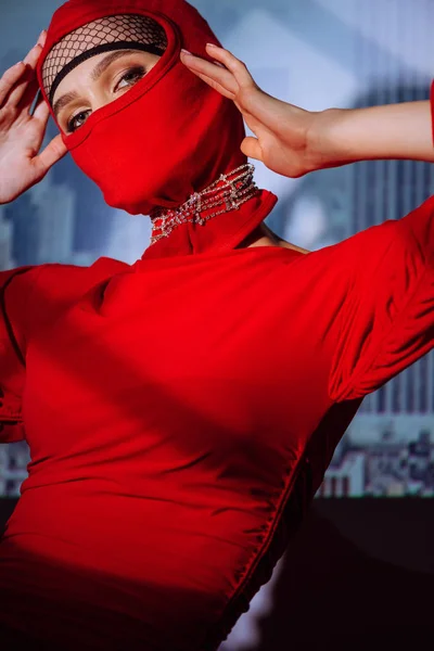 Stylische Frau in rotem Kleid und Sturmhaube auf Stadthintergrund — Stockfoto