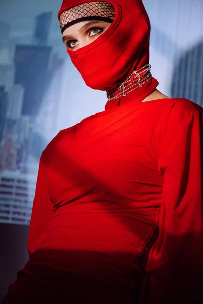 Mujer con estilo en vestido rojo y pasamontañas en el fondo de la ciudad - foto de stock