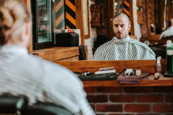 Selektiver Fokus eines gutaussehenden bärtigen Mannes, der im Friseurladen in den Spiegel schaut — Stockfoto