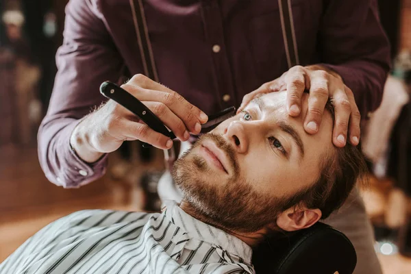 Selective focus of barber shaving handsome man — Stock Photo