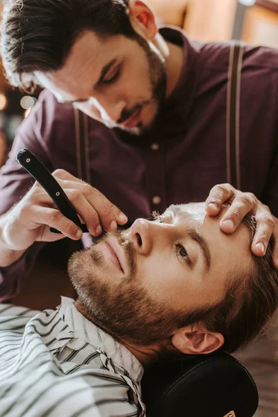 Избирательный фокус красивого парикмахера, бреющего бороду — стоковое фото