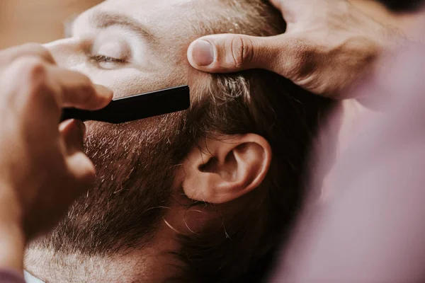 Vue recadrée de barbier rasage homme barbu avec rasoir — Photo de stock