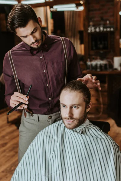 Stilvoller Friseur mit Rasiermesser und steht neben bärtigem Mann im Friseursalon — Stockfoto