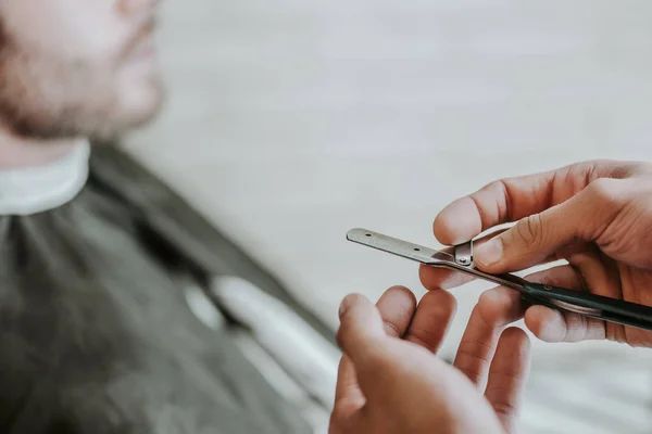 Cropped view of barber holding razor near man in barbershop — Stock Photo