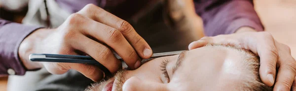 Colpo panoramico di barbiere tenuta rasoio durante la rasatura uomo — Foto stock