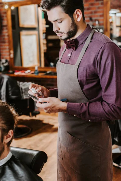 Beau et élégant coiffeur tenant pulvérisation antibactérienne près du rasoir — Photo de stock