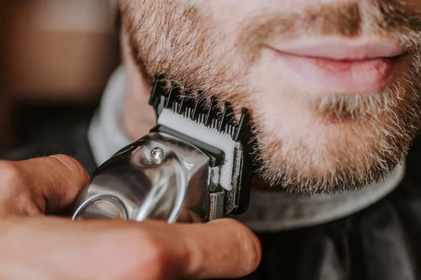 Крупним планом перукар тримає тример під час гоління чоловіка — стокове фото