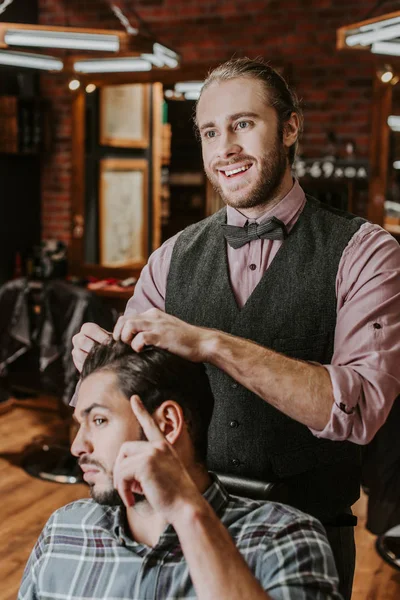 Barbeiro alegre styling cabelo no homem barbudo bonito — Fotografia de Stock