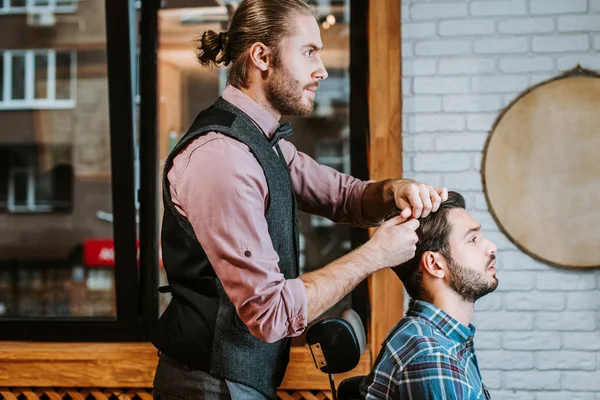 Side view of barber styling hair on cheerful bearded man — Stock Photo