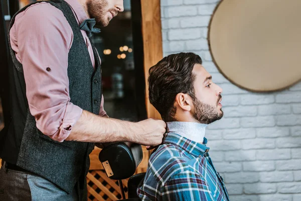 Seitenansicht des Friseurs Befestigung Kragen um den Hals des glücklichen Mannes — Stockfoto