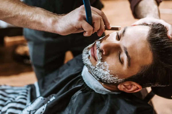 Barber shaving bearded man with shaving cream on face — Stock Photo