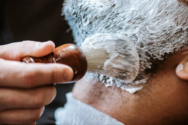 Primer plano de peluquero aplicando crema de afeitar en la cara del hombre - foto de stock