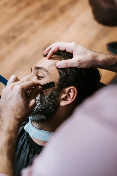 Enfoque selectivo de peluquero afeitado hombre con crema de afeitar en la cara - foto de stock