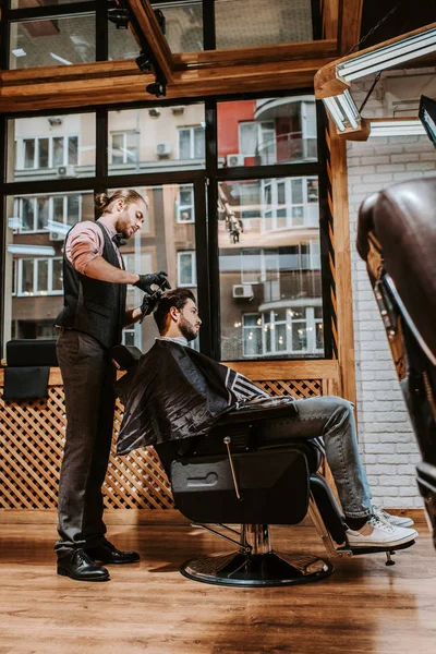 Side view of handsome barber styling hair of man in modern barbershop — Stock Photo