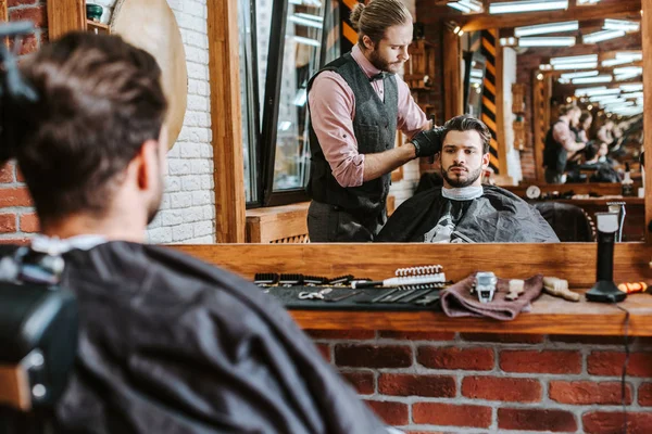Messa a fuoco selettiva di bello barbiere styling capelli dell'uomo vicino specchio in barbiere — Foto stock
