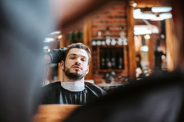 Selective focus of barber styling hair of bearded man near mirror in barbershop — Stock Photo