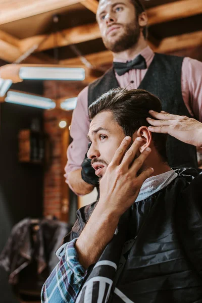 Foyer sélectif de bel homme touchant les cheveux près du coiffeur — Photo de stock