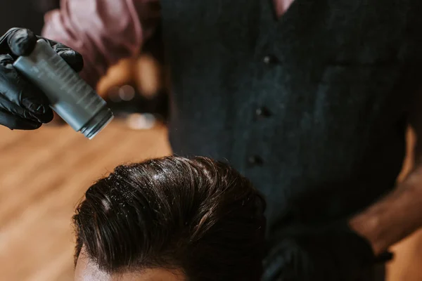 Vue recadrée du barbier tenant bouteille avec poudre au-dessus de la tête de l'homme dans le salon de coiffure — Photo de stock
