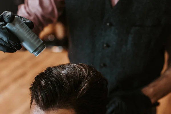 Cropped view of barber holding bottle with powder above head of man in barbershop — Stock Photo