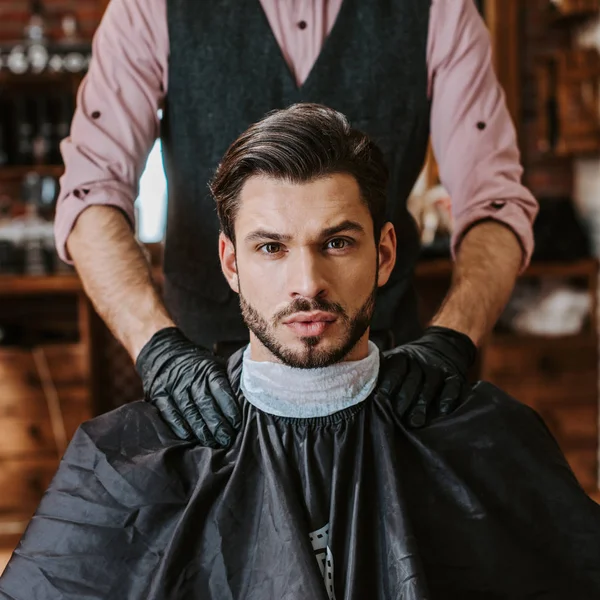 Barbeiro em luvas de látex preto colocando as mãos sobre ombros de homem na barbearia — Fotografia de Stock