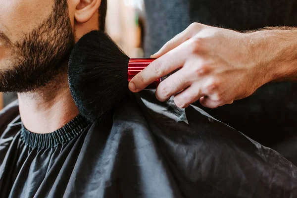 Cropped view of barber holding cosmetic brush near face of happy bearded man — Stock Photo