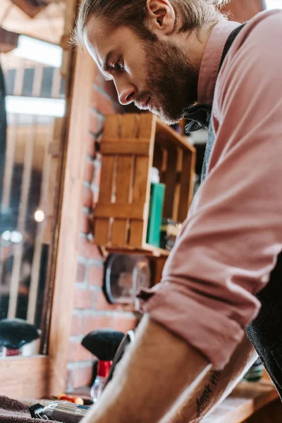 Vista lateral de barbeiro bonito em pé na barbearia — Fotografia de Stock