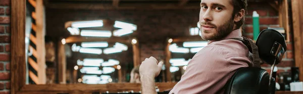 Panoramic shot of handsome and bearded barber looking at camera — Stock Photo