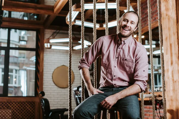 Hombre barbudo feliz mirando a la cámara y sonriendo en la barbería - foto de stock