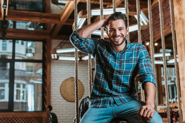 Happy man touching hair and looking at camera in barbershop — Stock Photo