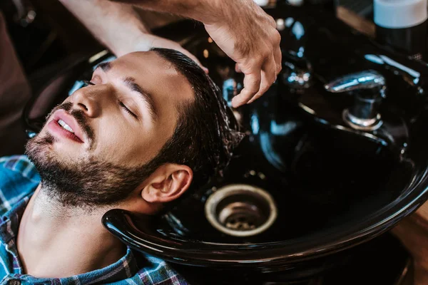 Barbeiro lavar o cabelo do homem barbudo na pia preta — Fotografia de Stock