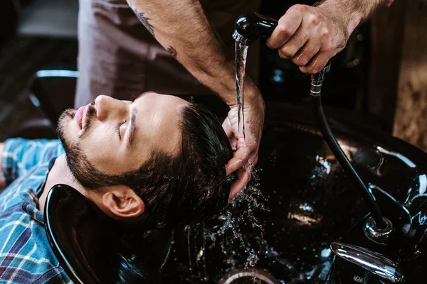 Parrucchiere tatuato lavare i capelli dell'uomo nel lavandino nero — Foto stock