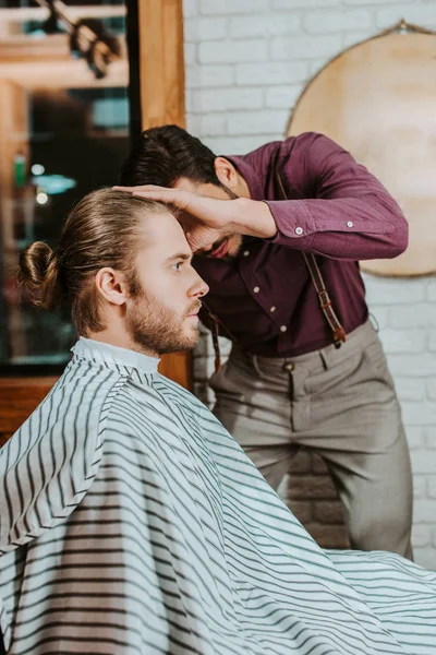 Barber styling hair of bearded man in barbershop — Stock Photo