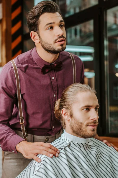 Bonito barbeiro de pé perto barbudo homem no barbearia — Fotografia de Stock