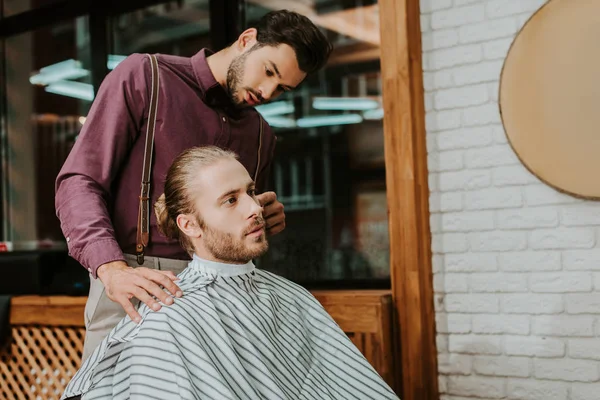 Barbeiro bonito olhando para o homem barbudo na barbearia — Fotografia de Stock