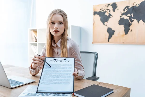 Attrayant agent de voyage pointant avec stylo au contrat sur presse-papiers — Photo de stock