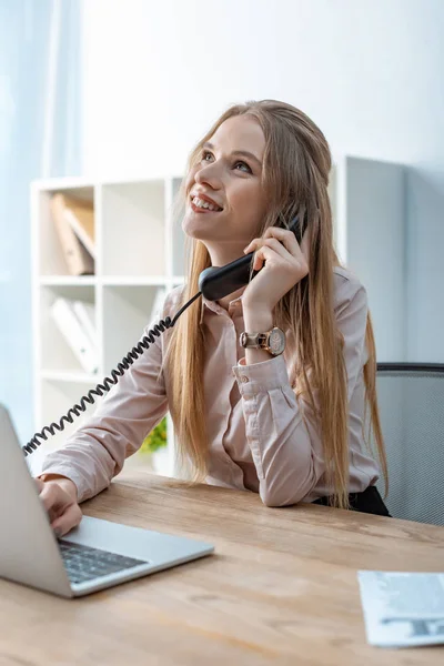 Smiling travel agent talking on phone while sitting at workplace — Stock Photo