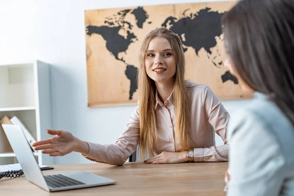 Smiling travel agent talking to client and pointing at laptop screen — Stock Photo