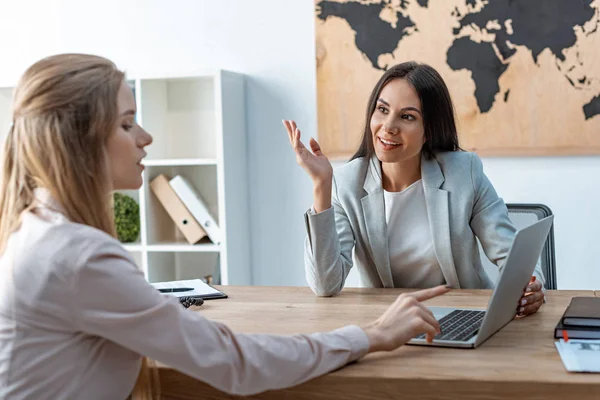 Smiling travel agent talking to client pointing with finger at laptop screen — Stock Photo